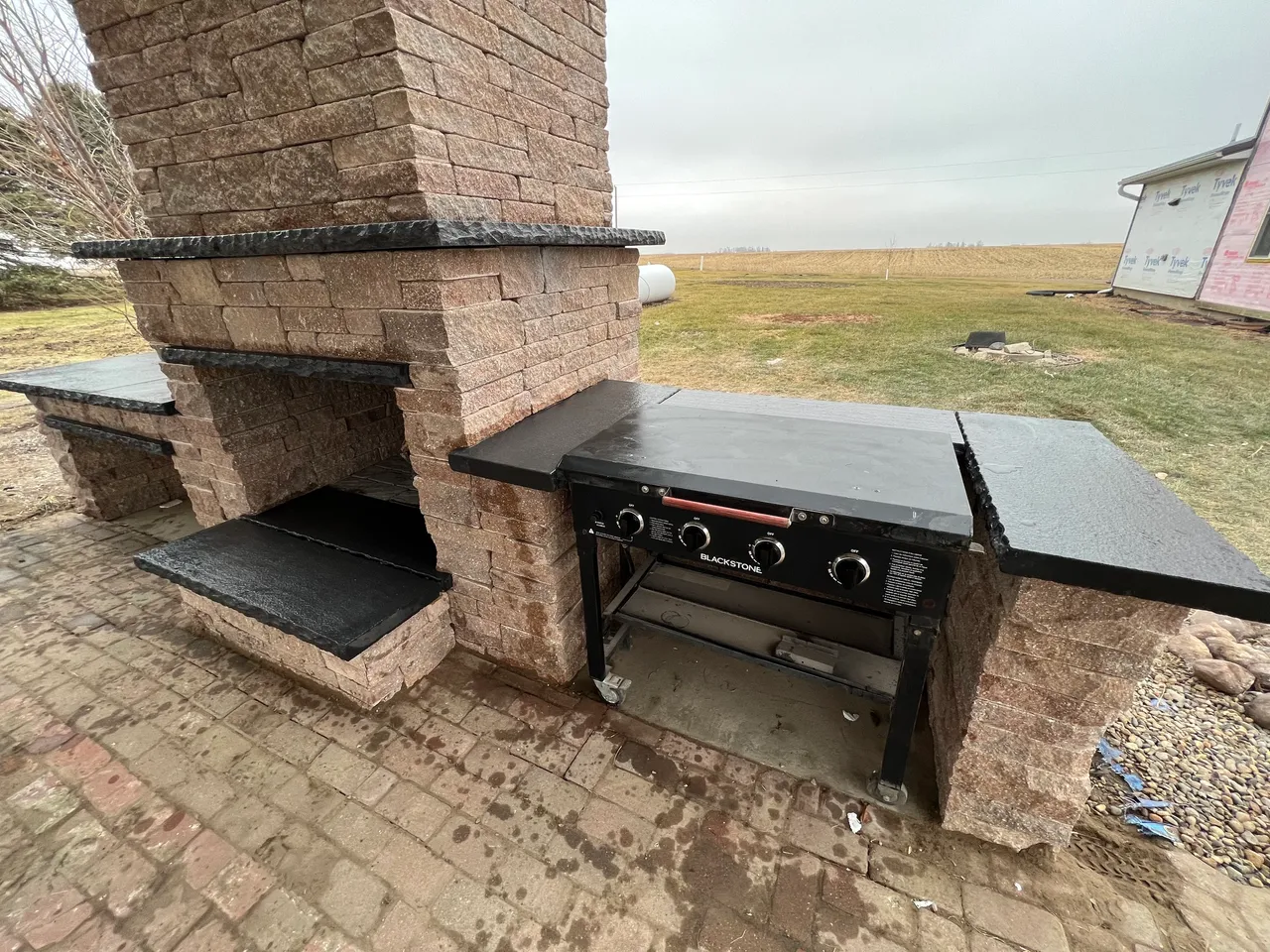 A grill and fireplace in the middle of an outdoor patio.
