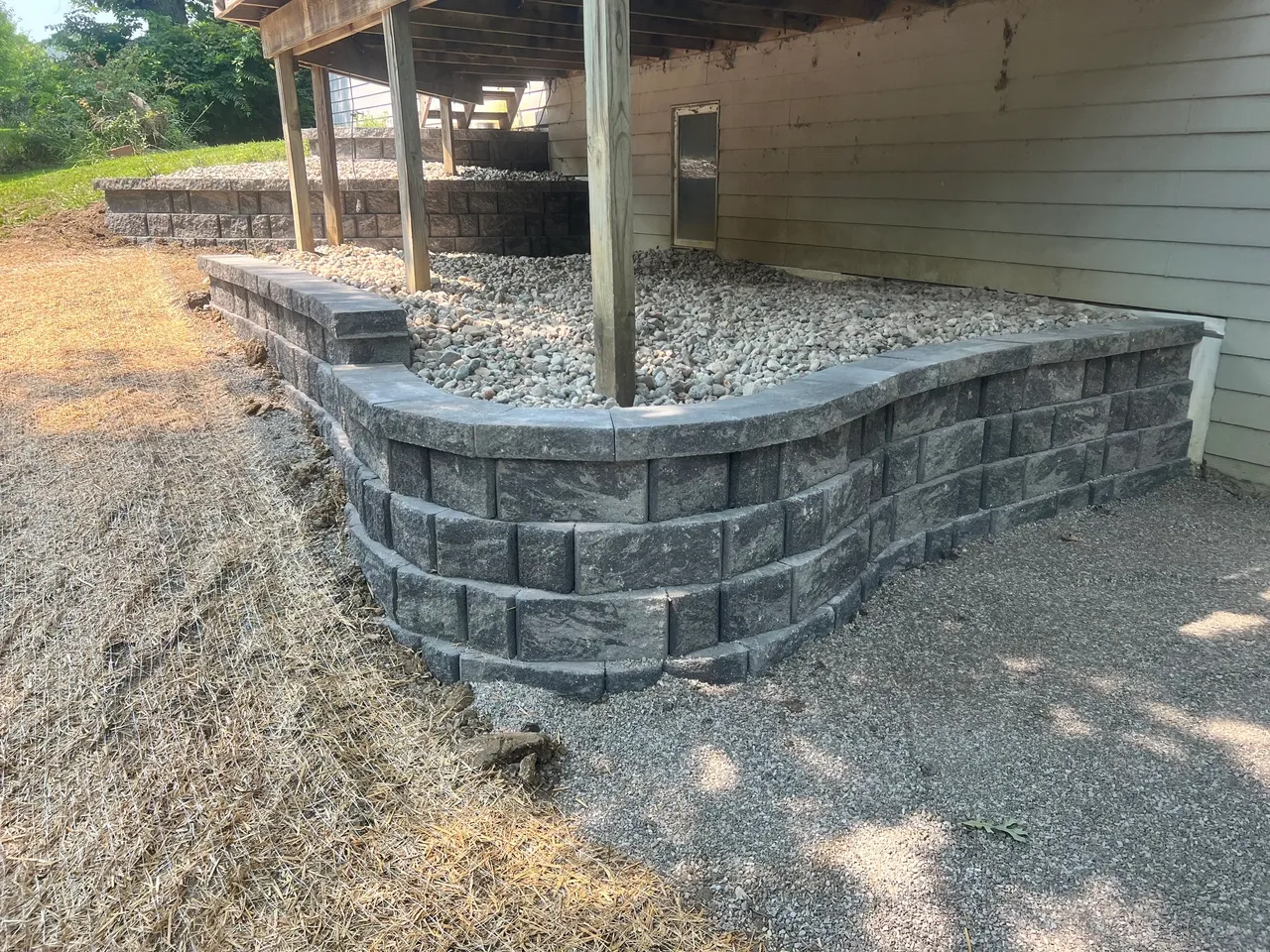 A brick wall with a concrete base and gravel on the side.