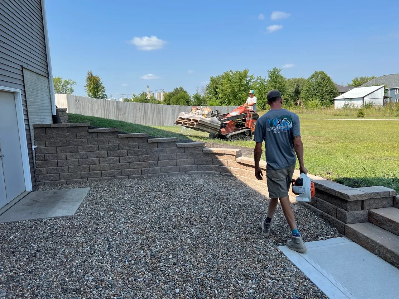 A man walking on gravel near a wall.