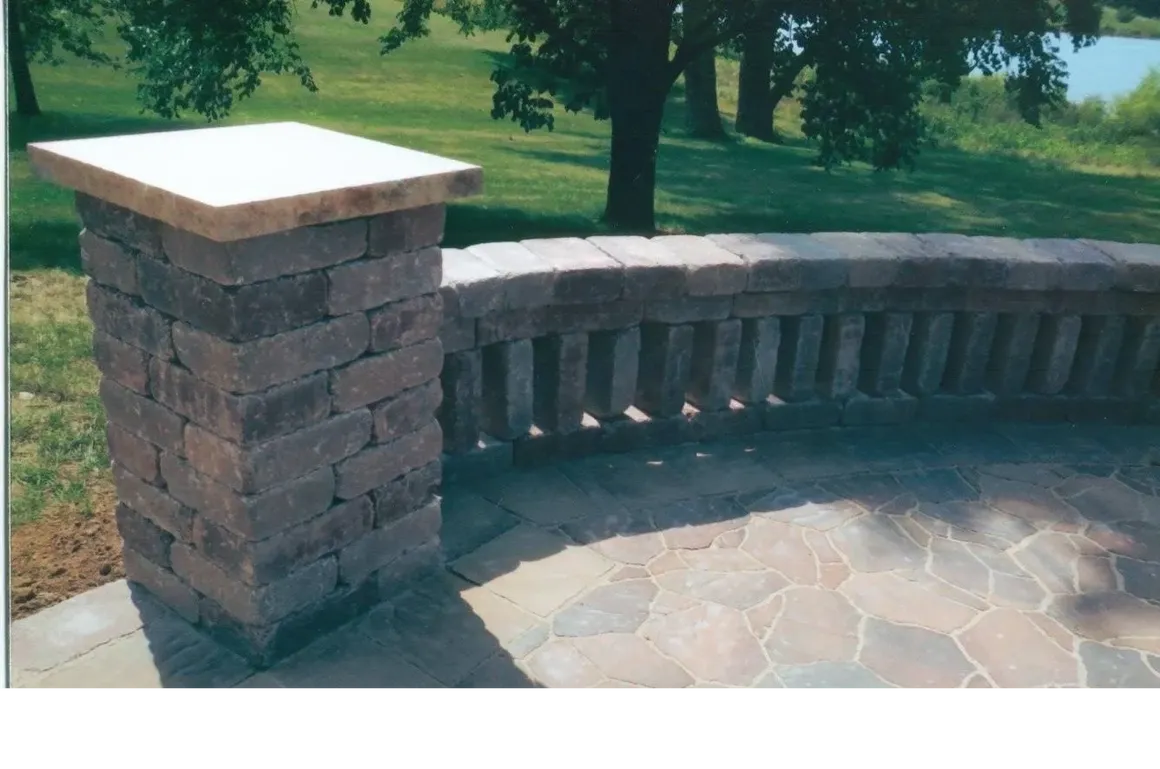 A stone wall with a brick pillar and a circular patio.